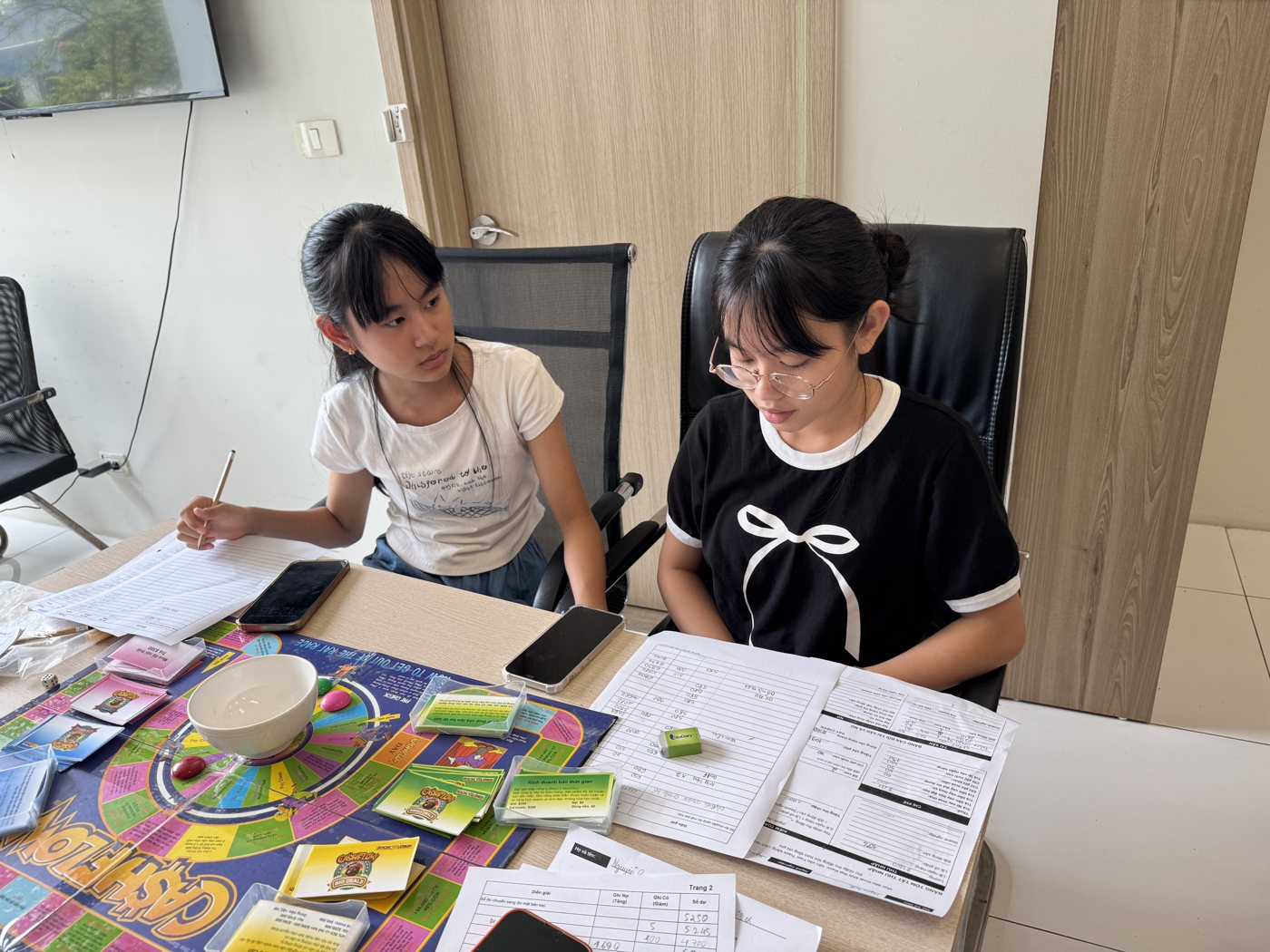 Hai bạn nhỏ tự tay điền bảng báo cáo tài chính bên bàn cờ Cashflow
