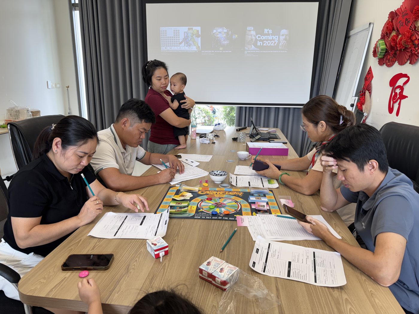 Bốn người lớn ngồi quanh bàn cờ Cashflow điền bảng báo cáo tài chính trong buổi luyện tập tại văn phòng